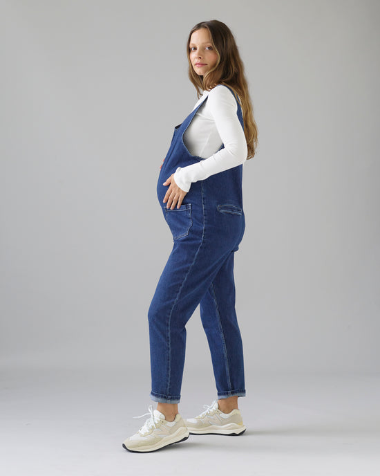 pregnant model wears mid blue denim lola jumpsuit