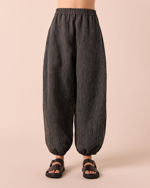 model wears logan black and ecru pencil stripe linen trousers. 