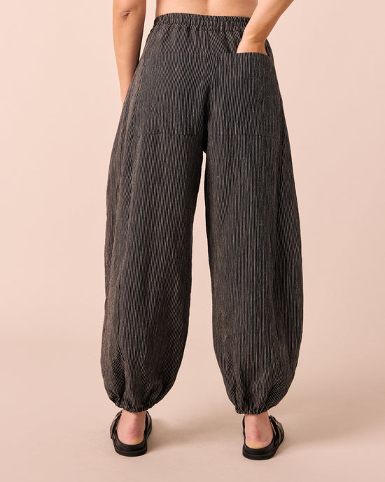 model wears logan black and ecru pencil stripe linen trousers. 