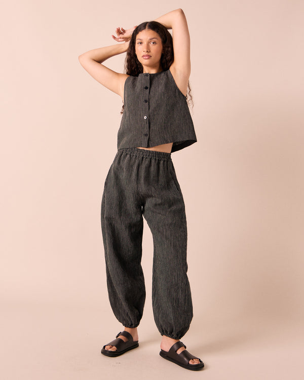 model wears logan black and ecru pencil stripe linen trousers. 
