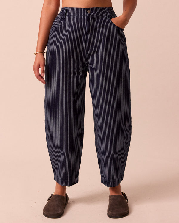 model wears remi navy pinstripe denim trousers left